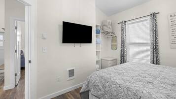 A bedroom with a bed, a television, a wardrobe, and a window with patterned curtains.
