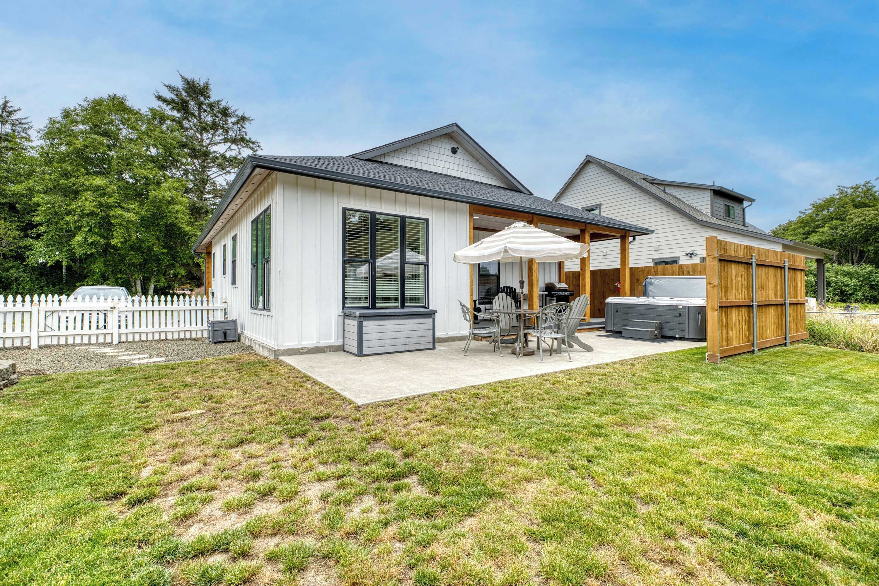 Ein modernes, zweistöckiges Haus mit einer Terrasse, einer überdachten Sitzgelegenheit und einem Holzzaun.