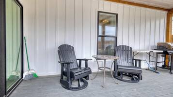 Un porche techado con sillas Adirondack, una mesita y una zona de barbacoa.