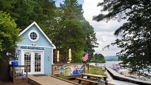 Un piccolo edificio blu con la scritta 'The Boat House' e un molo che si estende in un lago, circondato da alberi.