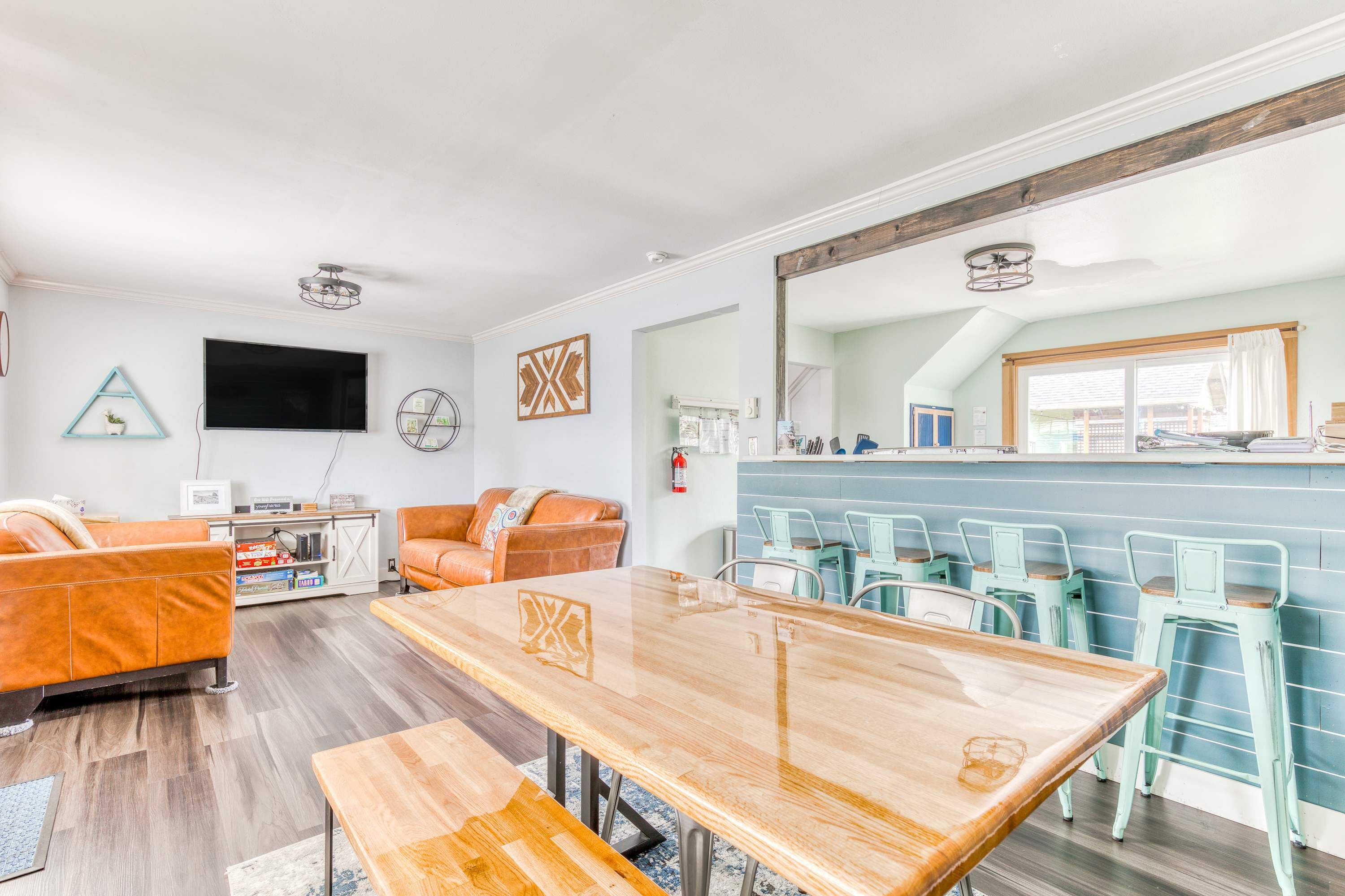 Uma sala de estar moderna com uma mesa de jantar de madeira, dois sofás de couro, uma televisão de tela plana e uma cozinha com banquetas.