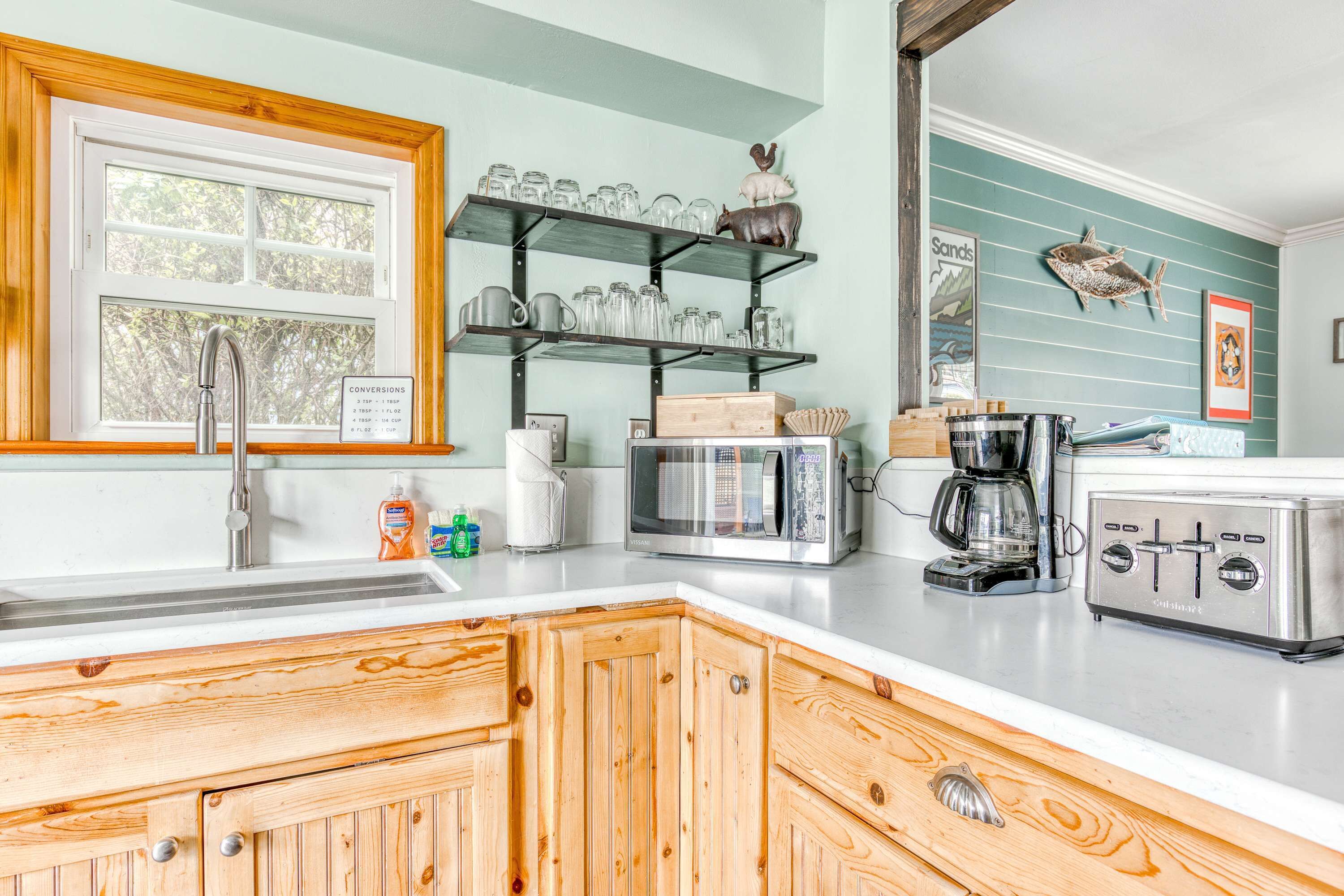 A kitchen with wooden cabinets, a stainless steel sink, a microwave, a toaster, and shelves with kitchenware.