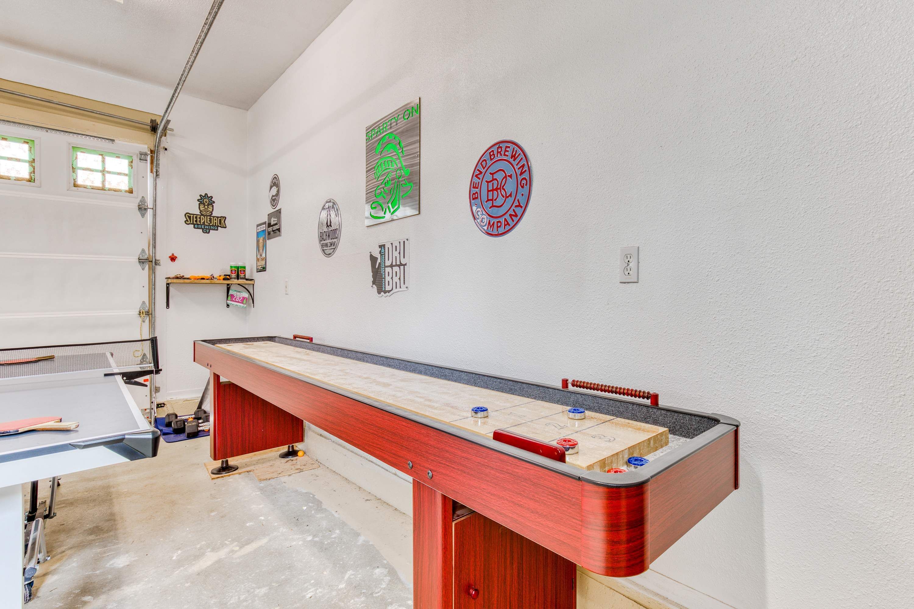 Une pièce équipée d’une table de billard, d’une porte de garage et de divers éléments de décoration murale, notamment des logos et une horloge.