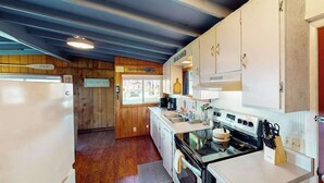 Eine kleine Küche mit Holzwänden, einem Kühlschrank, einem Herd und einem Spülbecken.