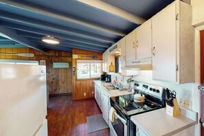 A compact kitchen with wooden walls, a refrigerator, a stove, and a sink. - Cottage with Panoramic Ocean Views in Quiet Area - Dogs OK (Yachats)
