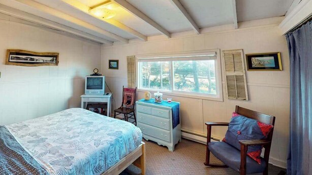 Ein Schlafzimmer mit Bett, Schreibtisch mit Computer, Stuhl, Kommode und Fenster mit Rollläden.