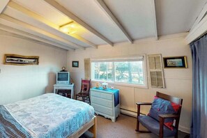 Un dormitorio con cama, escritorio con computadora, silla, cómoda y ventana con contraventanas.