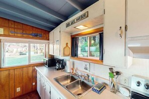 A kitchen with a double sink, a coffee maker, and a window with a view of the outdoors. - Cottage with Panoramic Ocean Views in Quiet Area - Dogs OK (Yachats)