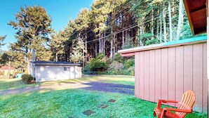 Ein Wohnhaus mit kleiner Gartenhütte, einer überdachten Terrasse mit zwei Adirondack-Stühlen und einem gepflegten Rasen.