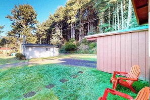 A residential property with a small shed, a covered patio area with two Adirondack chairs, and a well-maintained lawn. - Cottage with Panoramic Ocean Views in Quiet Area - Dogs OK (Yachats)