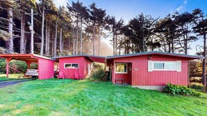 Eine rote Holzhütte mit Veranda und einem kleinen Anbau, umgeben von einem Wald.