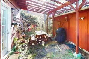 A covered outdoor area with a wooden table and benches, a barbecue grill, and a netted area with various items. - Cottage with Panoramic Ocean Views in Quiet Area - Dogs OK (Yachats)