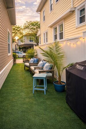 A backyard with artificial grass, a covered grill, and outdoor furniture. - Ventnor Seaside Gem: Outdoor Shower, Walk to Beach (Ventnor City)