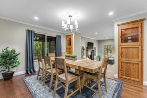 A dining area with a wooden table and chairs, a chandelier, and a large wooden cabinet. - Expansive retreat with pool, private hot tub, fast WiFi, fitness bike & SHARC (Sunriver)