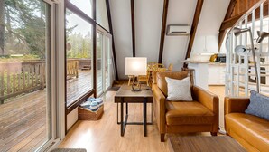 An interior with a wooden deck, a sofa, a table with a lamp, and a kitchen area. - Dog-Friendly Home with Expansive Deck with Hot Tub and Dock on Woahink Lake (Florence)