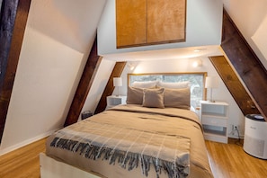A bedroom with a bed, nightstands, a heater, and a window with a view.
