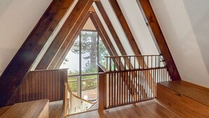 A wooden staircase with a railing leading to a balcony with a view of trees and a body of water. - Dog-Friendly Home with Expansive Deck with Hot Tub and Dock on Woahink Lake (Florence)