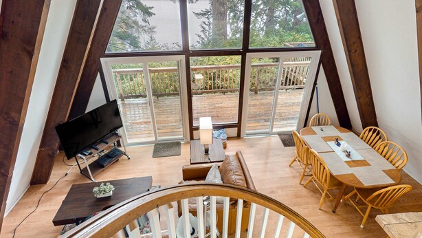 A room with a large window, wooden furniture, a TV, and a dining table. - Dog-Friendly Home with Expansive Deck with Hot Tub and Dock on Woahink Lake (Florence)