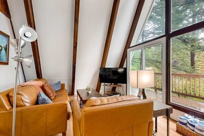 Un salon confortable avec un canapé, une télévision, une lampe et une grande fenêtre donnant sur une terrasse.