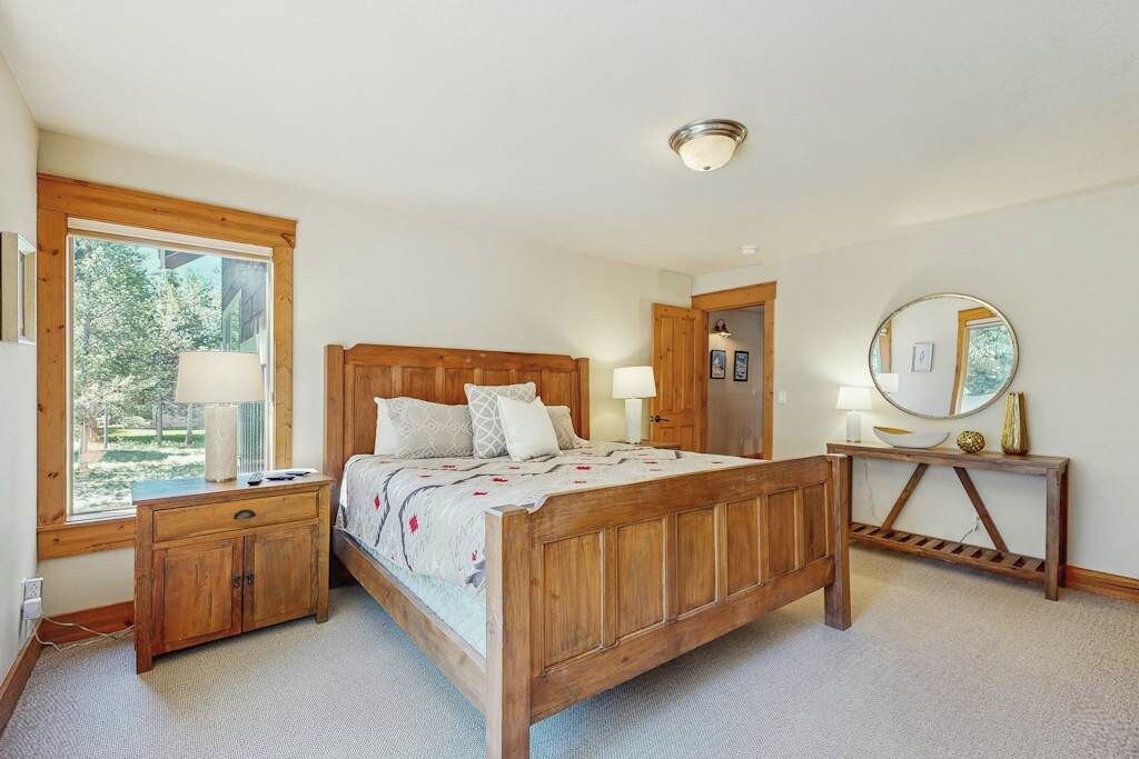 A bedroom with a wooden bed, bedside tables, a mirror, and a window with a view of trees.