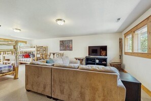 A spacious living area with a sofa, a television, and a fireplace. There are multiple seating options including a couch and a bed. - Lodge-style luxury in Sunriver - hot tub, fireplace, gas grill, games (Sunriver)