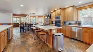 A modern kitchen with wooden cabinets, a central island with stools, a dishwasher, and a large window. - Lodge-style luxury in Sunriver - hot tub, fireplace, gas grill, games (Sunriver)