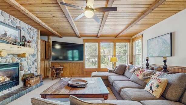 A cozy living room with a stone fireplace, a large flat-screen TV, a wooden ceiling, and a comfortable sofa. - Lodge-style luxury in Sunriver - hot tub, fireplace, gas grill, games (Sunriver)