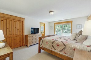 A bedroom with a bed, wooden wardrobe, television, dresser, and a window with a view. - Lodge-style luxury in Sunriver - hot tub, fireplace, gas grill, games (Sunriver)