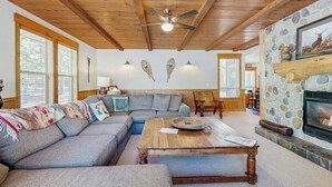 A cozy living room with a stone fireplace, wooden ceiling beams, and a large window. - Lodge-style luxury in Sunriver - hot tub, fireplace, gas grill, games (Sunriver)