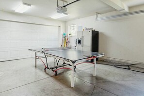 A ping pong table in a garage with a white door, a refrigerator, and a ceiling-mounted projector. - Lodge-style luxury in Sunriver - hot tub, fireplace, gas grill, games (Sunriver)