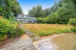 A house with a deck, surrounded by a forest and a stream.
