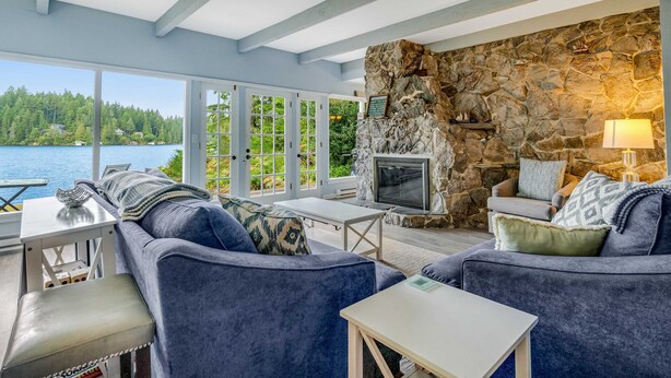 A room with a stone fireplace, a sofa, a TV, and a view of a lake.