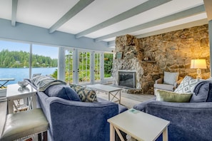 A room with a stone fireplace, a sofa, a TV, and a view of a lake.