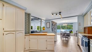 A modern kitchen with white cabinetry, a wooden countertop, and a dining area with a view.