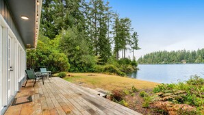 A wooden deck with outdoor furniture, a lake view, and a forested area.