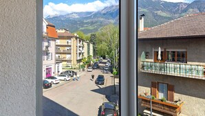 Vista de la calle con edificios, coches aparcados y montañas al fondo.
