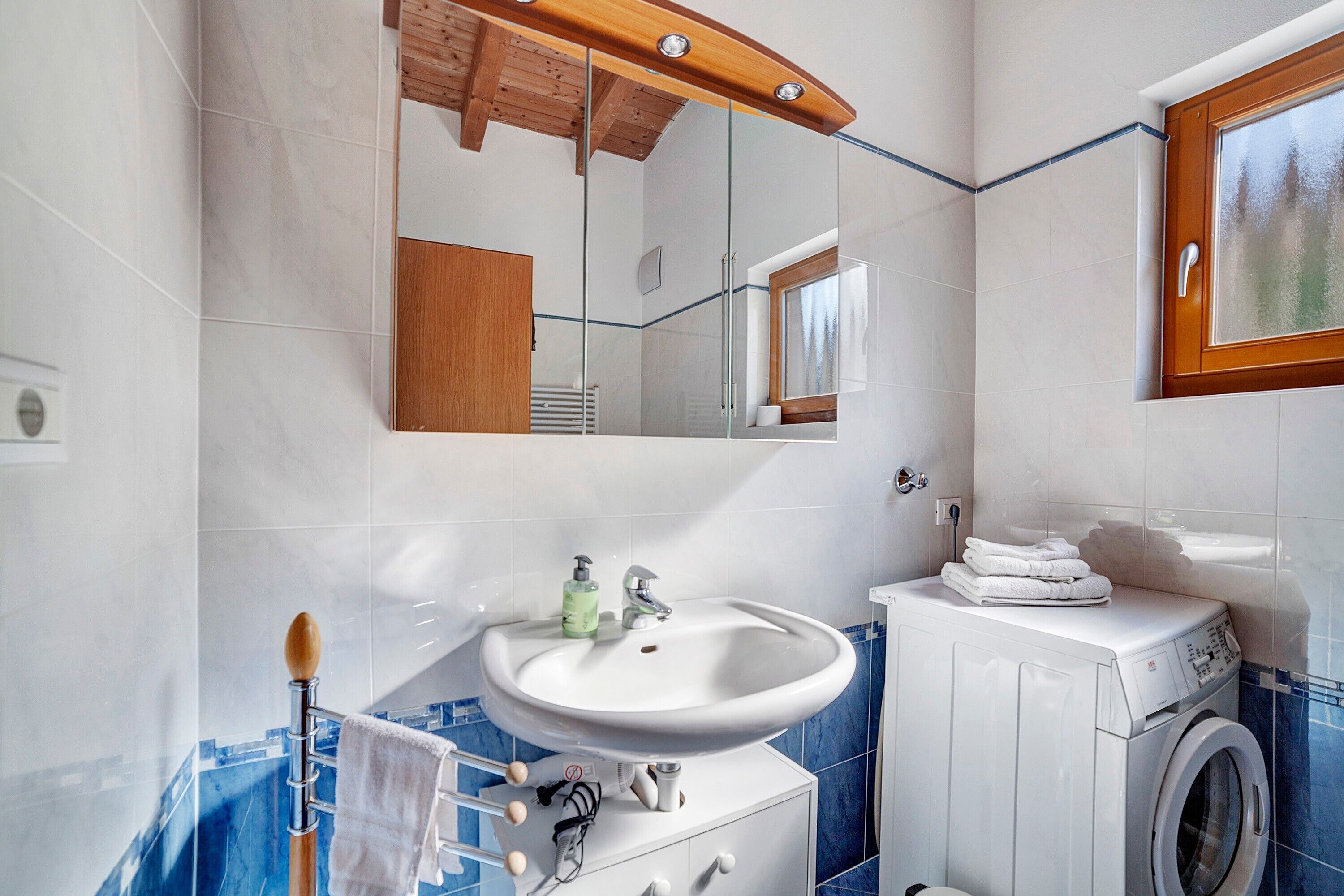 A bathroom with a sink, mirror, wooden ceiling, and a washing machine.