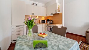 Un pequeño comedor con una mesa dispuesta para dos, un florero con flores y un cuenco de fruta.