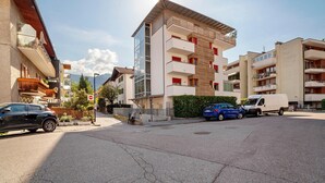 Un edificio residencial de varios pisos con balcones, una zona de estacionamiento y cielo despejado.