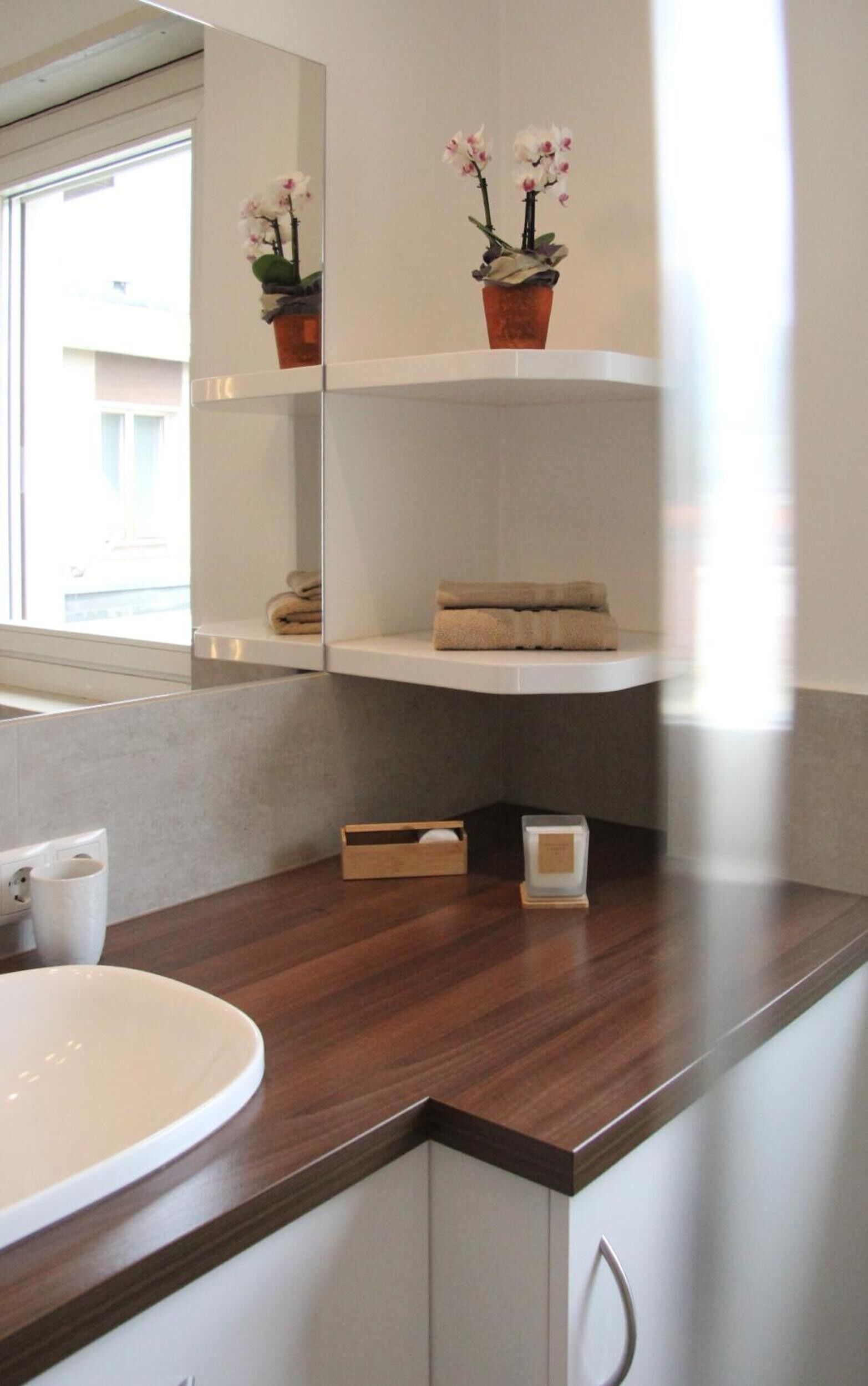 A bathroom with a wooden countertop, a white sink, a mirror, and a shelf with towels and flowers.