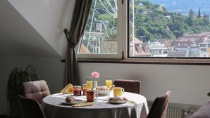 Un comedor con una mesa dispuesta para el desayuno, vistas a la montaña y una ventana con cortinas.