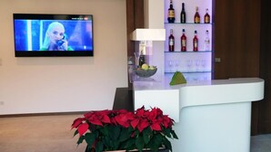 Un área de recepción con televisor, un bar con botellas de licores, un frutero y una planta en maceta.