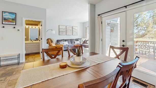 A dining area with a wooden table, chairs, a plant centerpiece, and a view to the outside.