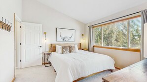 A bedroom with a bed, a coat rack, a door, a framed picture, and a window with blinds.