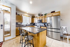 A modern kitchen with wooden cabinets, a stainless steel refrigerator, a built-in oven, and a central island with bar stools.
