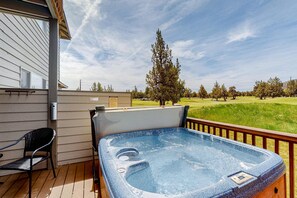 A hot tub on a wooden deck with a view of a grassy field and trees.