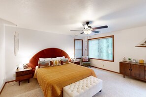 Une chambre à coucher avec un grand lit, un ventilateur de plafond, une table de chevet, une commode et une fenêtre avec des stores.
