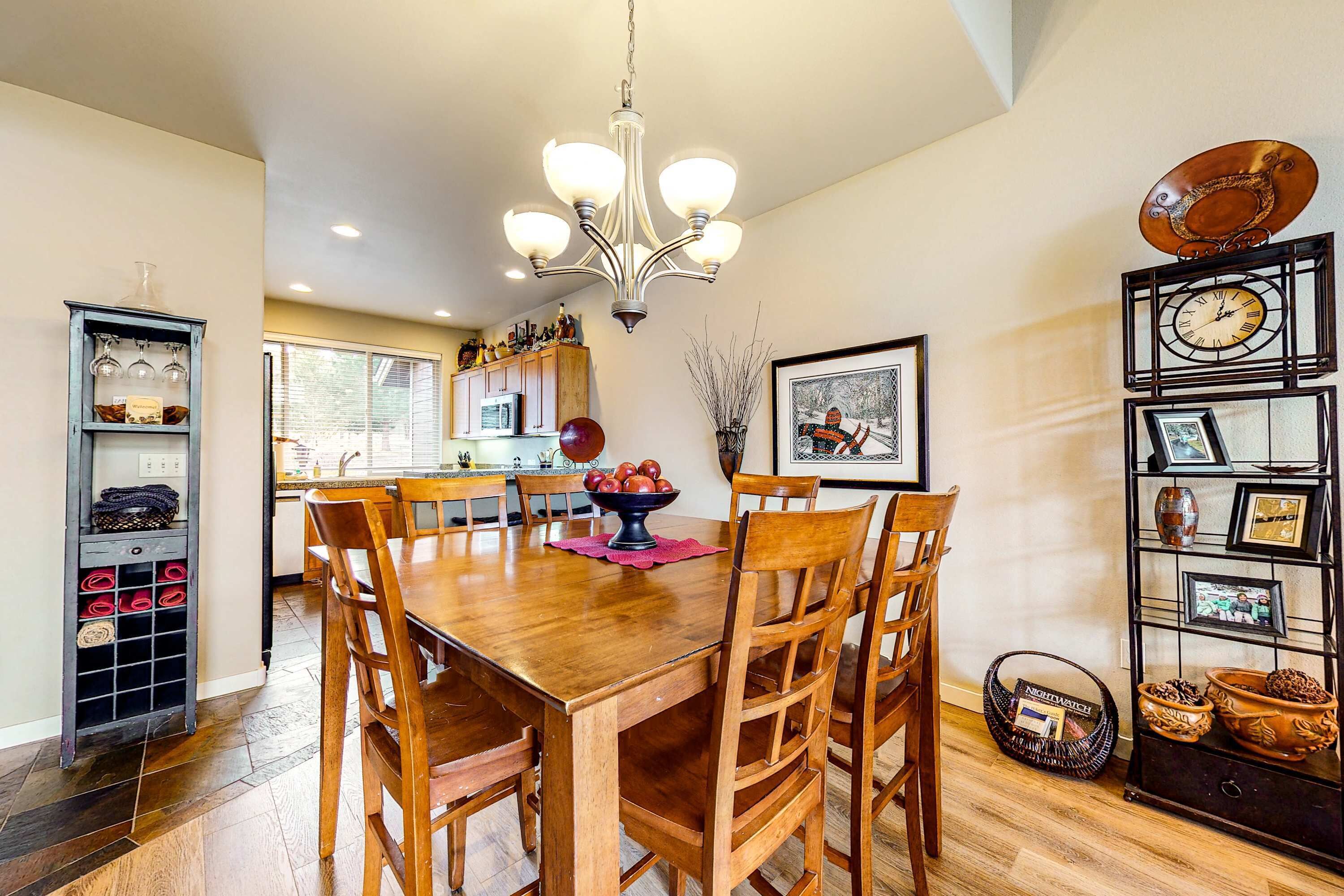 Un coin repas comprenant une table en bois, des chaises, un lustre, un meuble à vin et un mur décoré de tableaux encadrés.