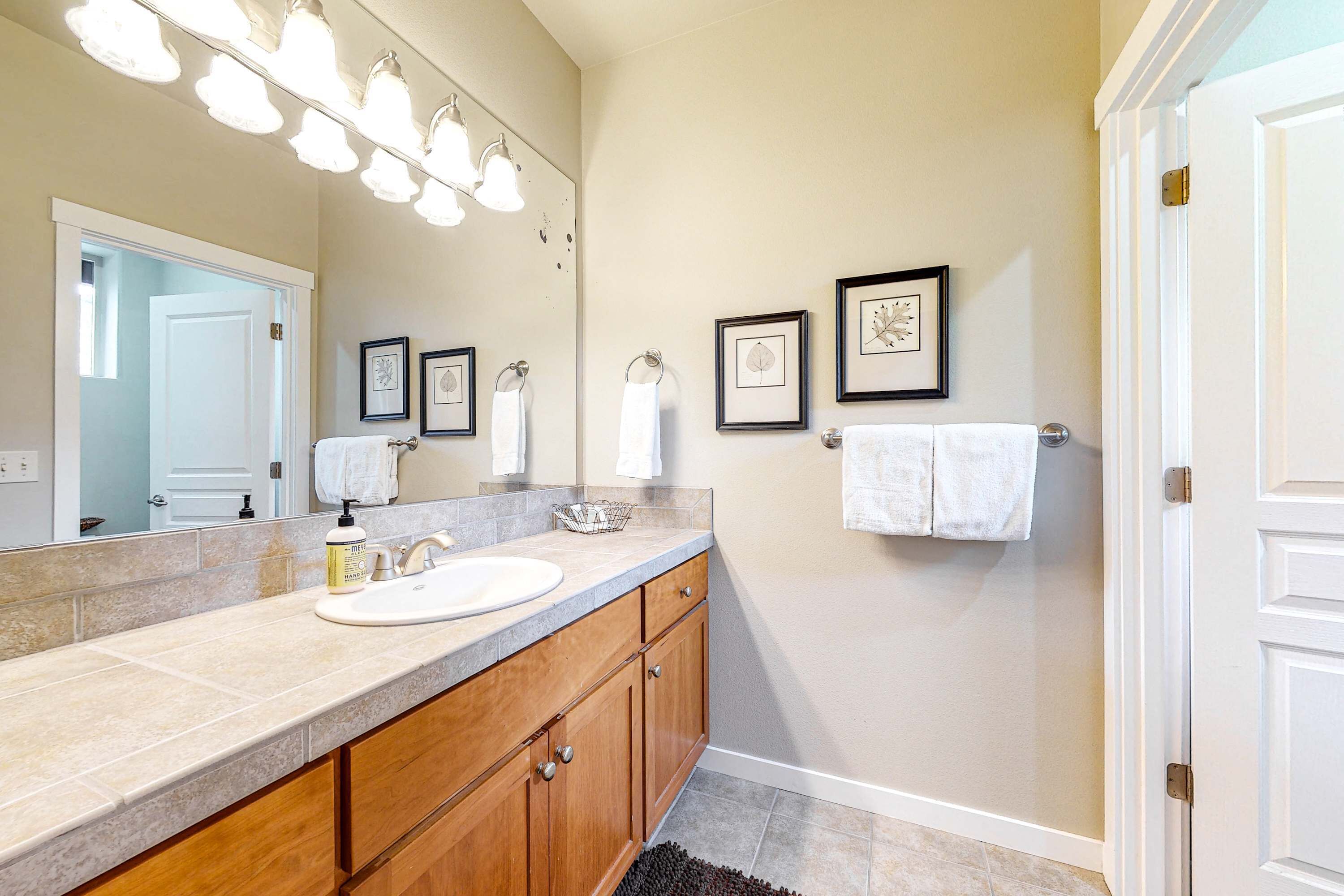 Une salle de bain avec un grand miroir, un lavabo, des meubles en bois et des œuvres d’art encadrées accrochées au mur.