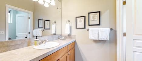 Une salle de bain avec un grand miroir, un lavabo, des meubles en bois et des œuvres d’art encadrées accrochées au mur.
